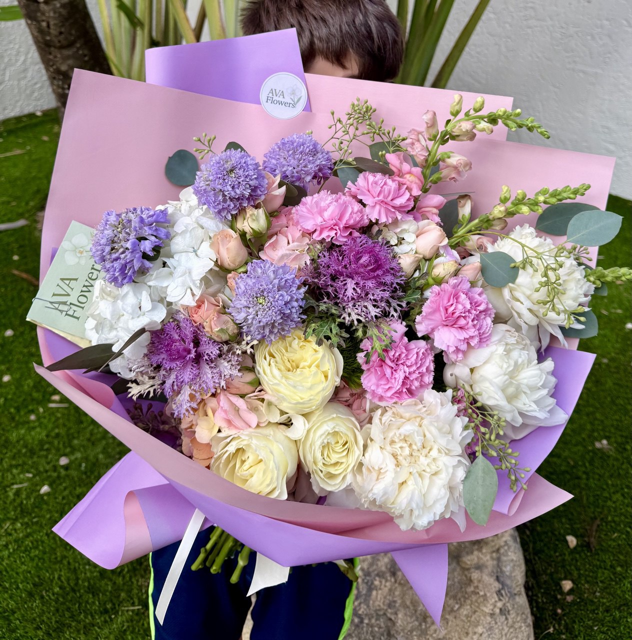 Bouquet of flowers wrapped in pink paper held by a person outdoors.