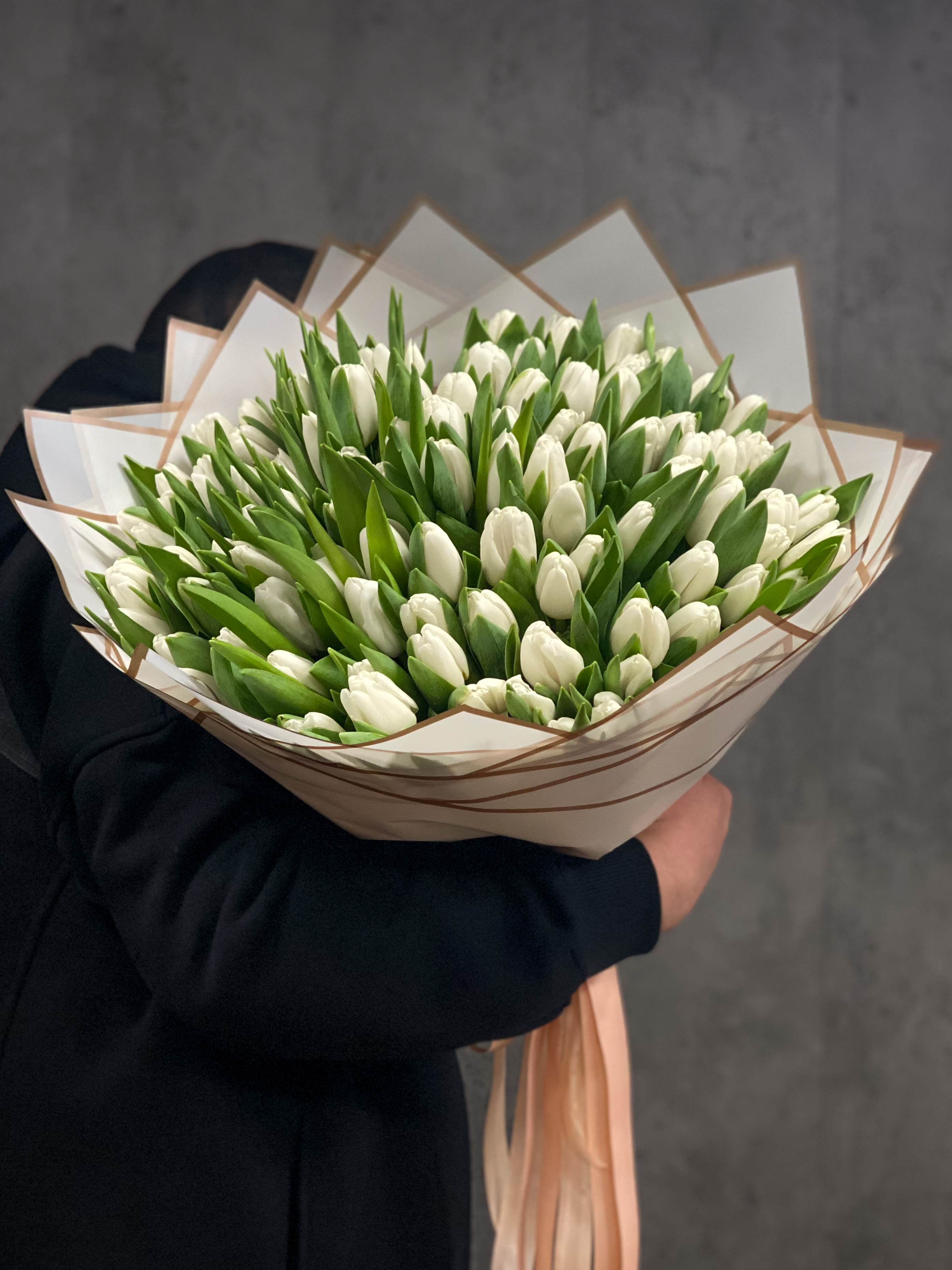 Bouquet of white tulips wrapped in brown paper with a plain background