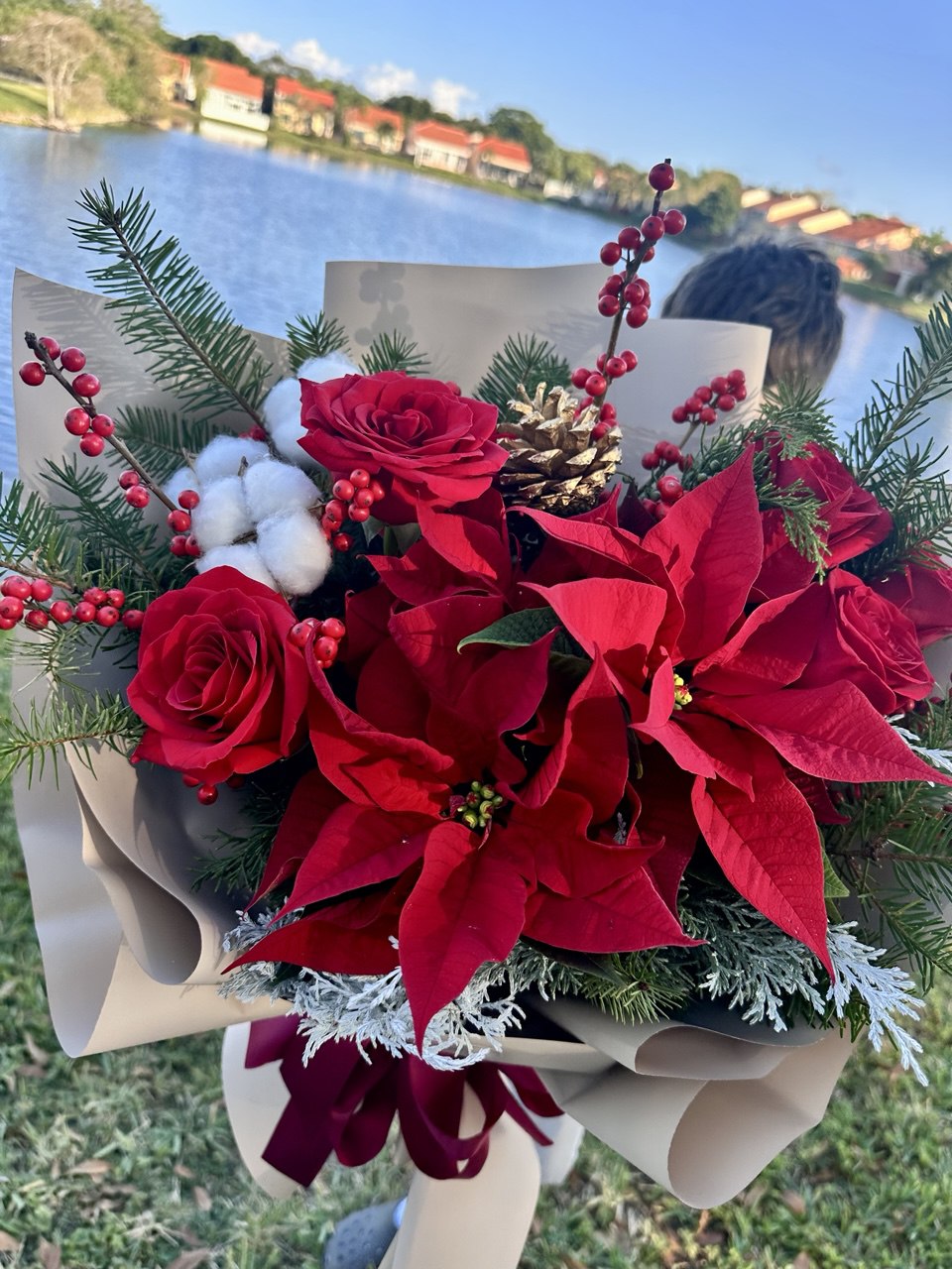 Bouquet of red flowers with poinsettias and greenery held by a person outdoors.