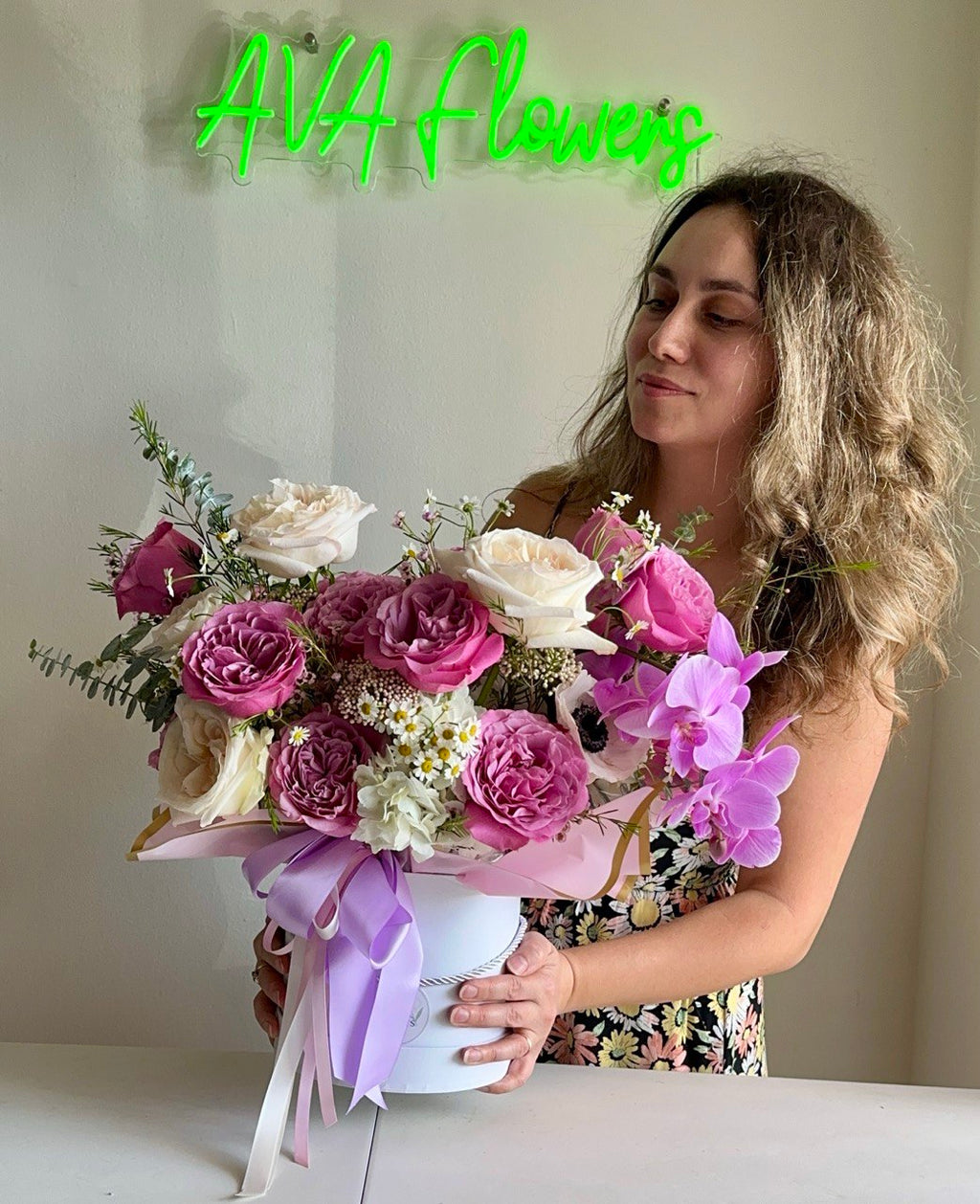 Aurora Hat Box flower arrangement with lush pink and cream roses, delicate orchids, anemones, chamomile, and eucalyptus greenery in an elegant white hat box tied with pastel ribbons — a luxurious floral gift
