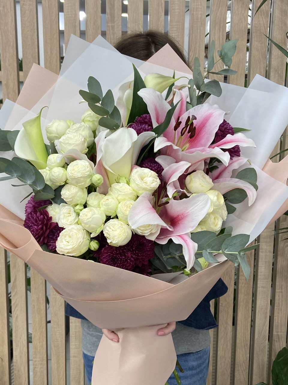 Lily’s Embrace bouquet with elegant pink lilies, delicate white spray roses, calla lilies, and lush eucalyptus, beautifully wrapped in pastel paper for a romantic and graceful floral arrangement