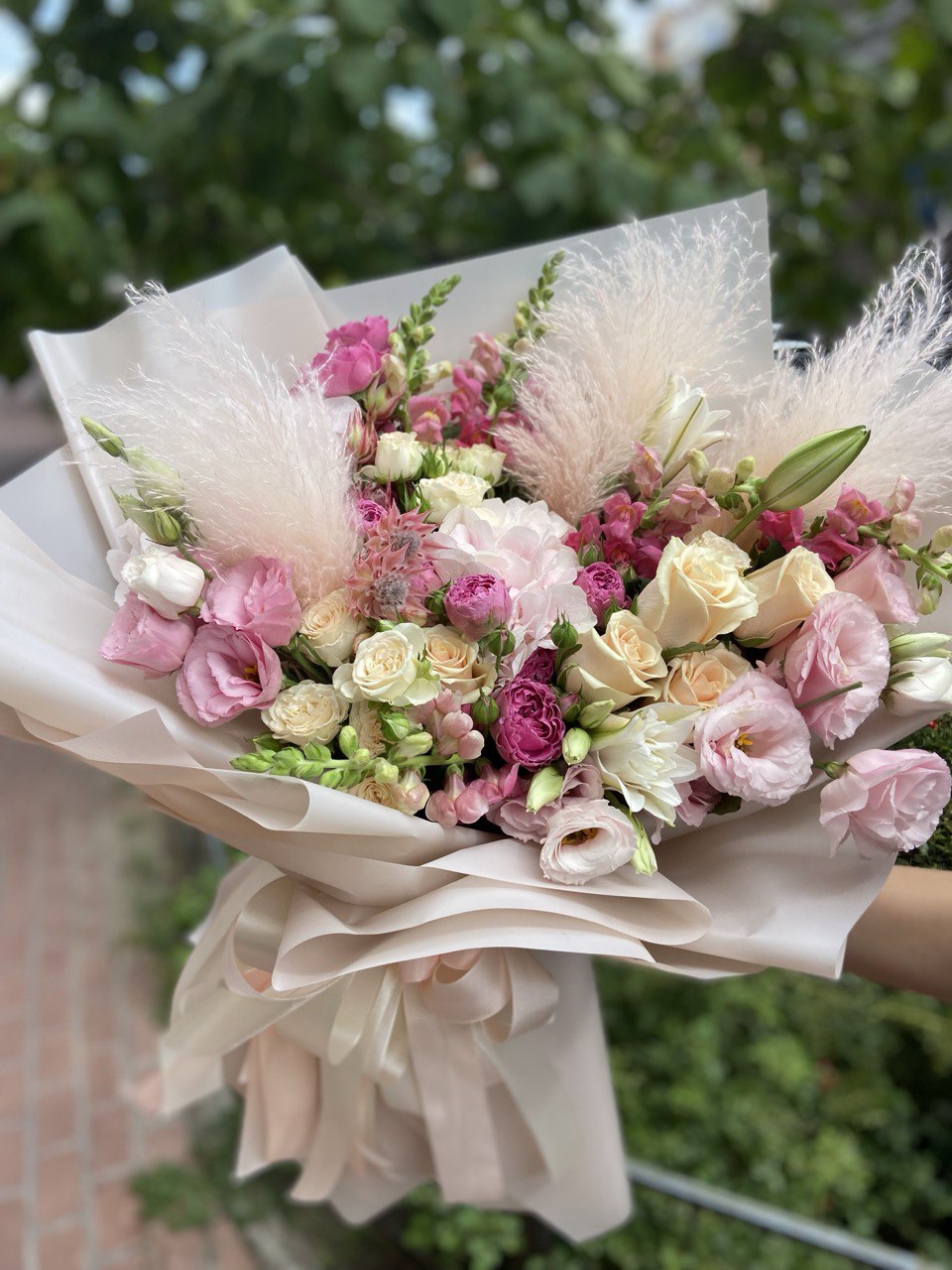 Tender Bliss bouquet with pastel roses, pink lisianthus, spray roses, lilies, and pampas grass wrapped in soft beige paper with satin ribbons — a delicate and romantic floral arrangement
